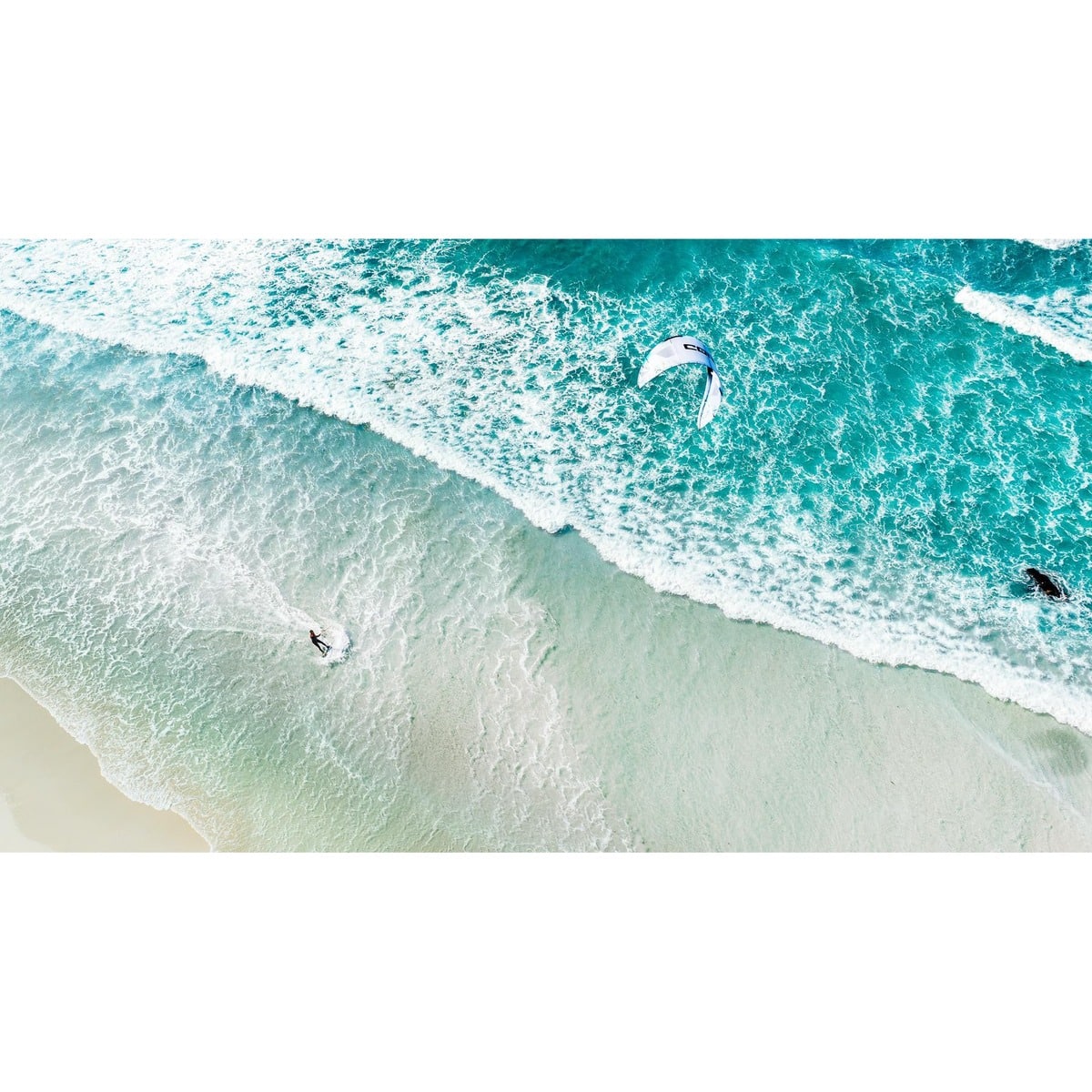 Aerial view of a person kite surfing on clear blue water near a beach.